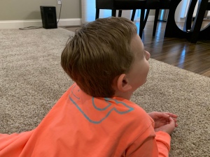 Child laying on the floor in an orange shirt with a blue whale on the back.